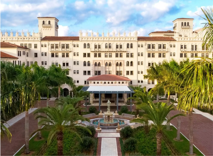 Wide view of The Boca Raton courtyard and facade with flanking palm trees.